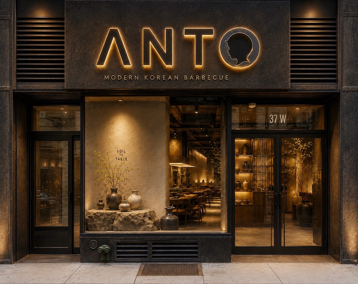 The Anto storefront at 37 W 32nd Street — a warm backlit sign in black stone above a softly lit window display of Korean pottery